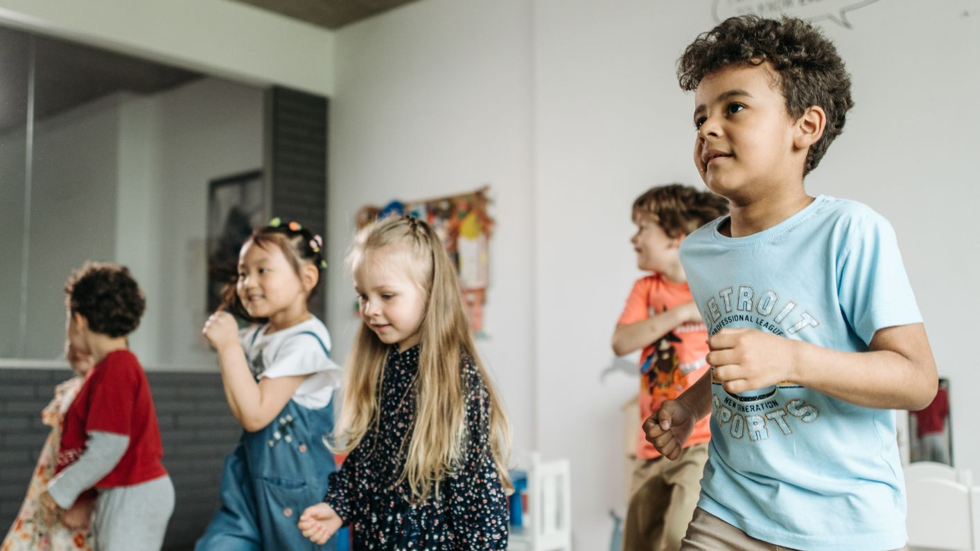 Kinder spielen in einem Klassenzimmer, während eine Lehrerin sie anleitet und beobachtet.