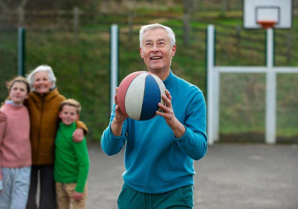 Ein älterer Mann präsentiert einen Basketball vor einer versammelten Gruppe.