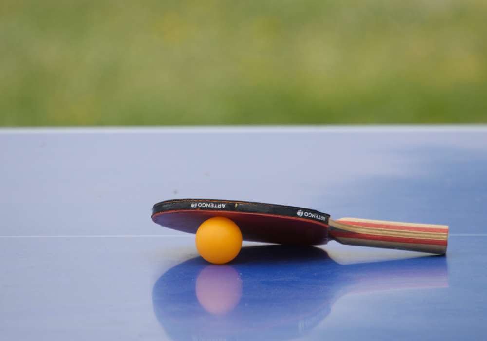 Ein Tischtennisschläger und ein Ball liegen auf einem Tisch.